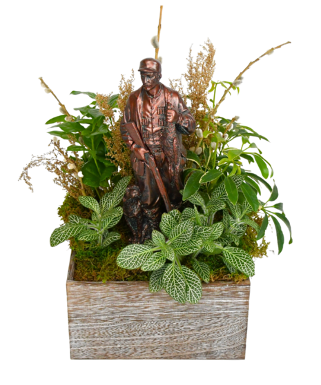 bronze model of a man sitting in a wooden box with green plants surrounding it