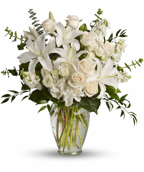 White and peach bouquet of lilies and roses with greenery in a clear glass vase