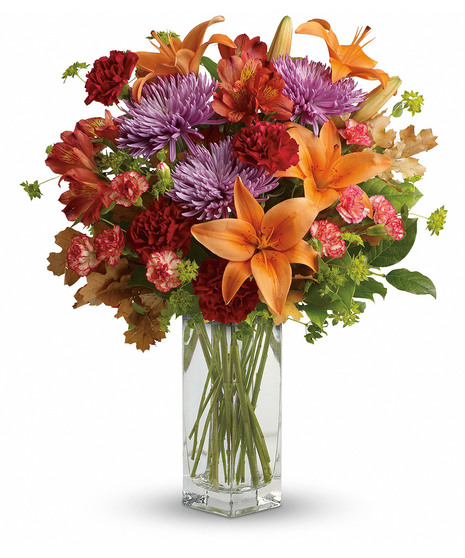 Orange lilies and red and lavender flowers in a tall rectangle vase