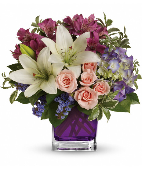 Purple hydrangea, light pink spray roses, and white asiatic lilies in a violet glass cube vase. 