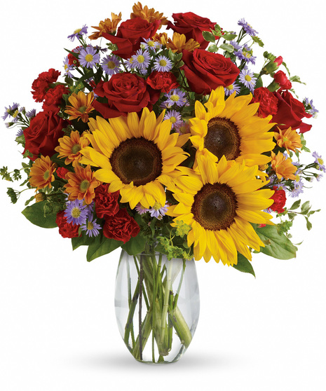 Clear glass vase of sunflowers, red roses, other flowers and greenery