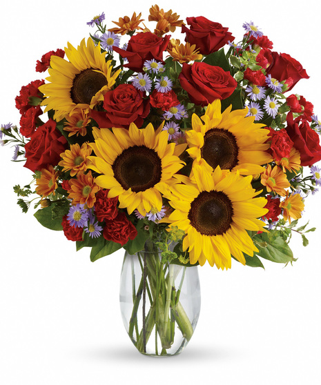 Clear glass vase of sunflowers, red roses, other flowers and greenery